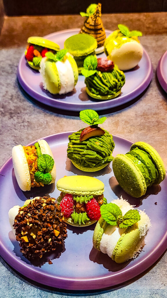 A view of 2 gray plates of a variety of gorgeous green matcha macaroon creations exquisitely decorated.