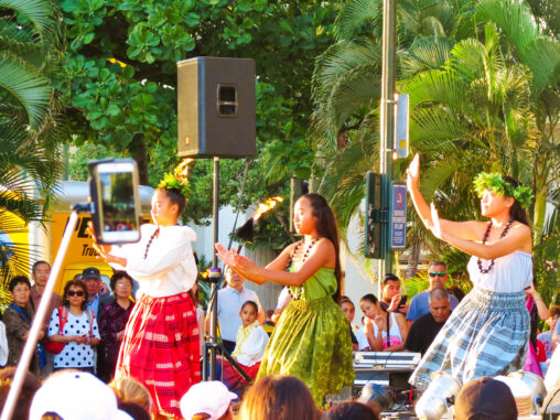Young female hula dancers performing on an open-air stage.
